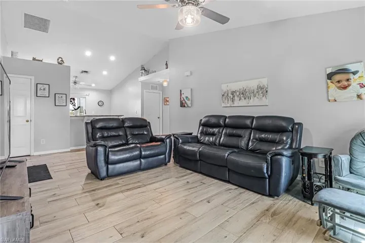 Living room featuring high vaulted ceiling, ceiling fan, and light wood-type flooring