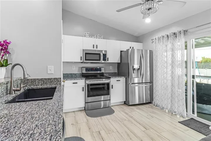 Kitchen featuring stainless steel appliances, ceiling fan, dark stone countertops, sink, and lofted ceiling