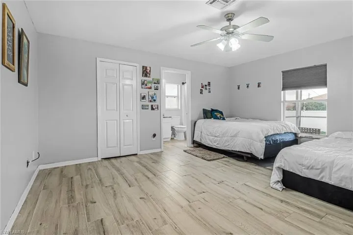 Bedroom with ceiling fan, ensuite bath, light hardwood / wood-style flooring, and a closet