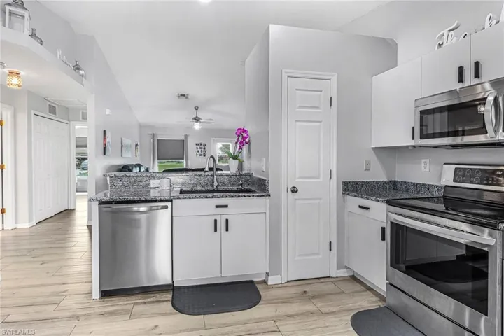 Kitchen featuring stainless steel appliances, dark stone countertops, white cabinetry, and ceiling fan
