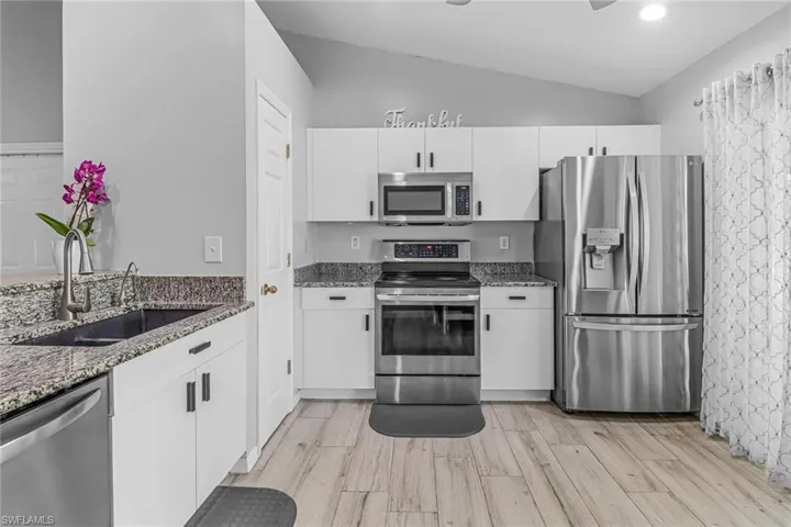 Kitchen featuring dark stone counters, light hardwood / wood-style flooring, stainless steel appliances, vaulted ceiling, and sink