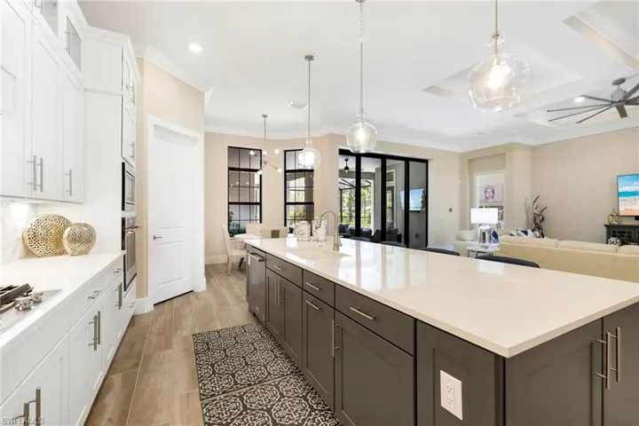 Kitchen featuring white cabinets, pendant lighting, coffered ceiling, light wood-type flooring, and sink