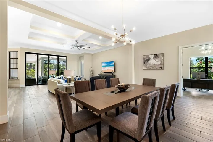 Dining space featuring light wood-type flooring, ceiling fan with notable chandelier, plenty of natural light, and coffered ceiling