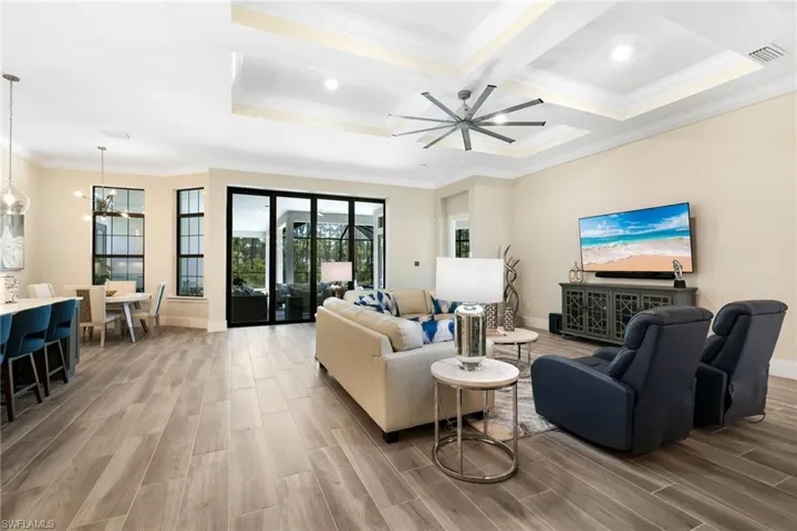 Living room featuring coffered ceiling, wood-type flooring, ceiling fan with notable chandelier, and ornamental molding