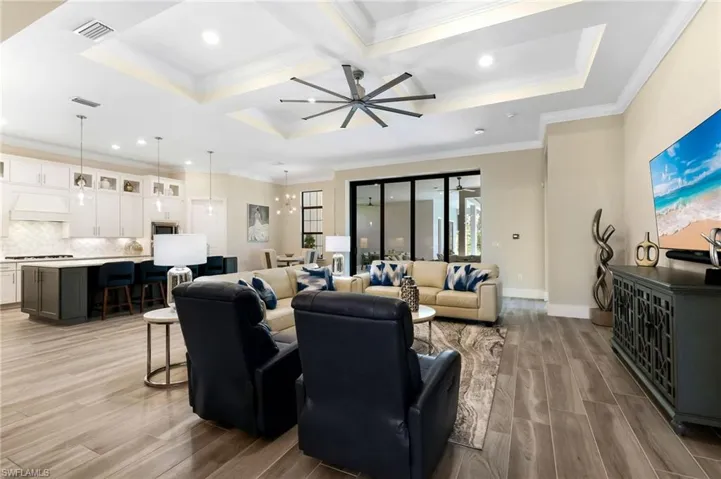 Living room featuring coffered ceiling, ceiling fan, ornamental molding, light hardwood / wood-style floors, and a raised ceiling