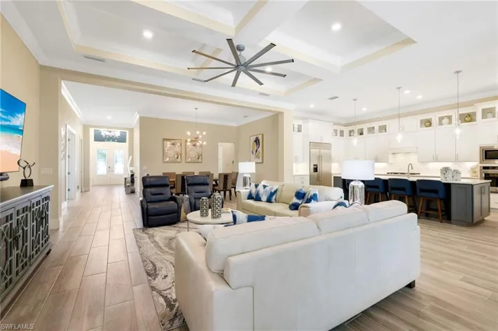 Living room with coffered ceiling, ceiling fan with notable chandelier, ornamental molding, light hardwood / wood-style flooring, and beamed ceiling