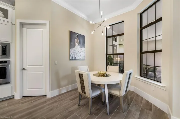 Dining area with wood-type flooring, a healthy amount of sunlight, ornamental molding, and an inviting chandelier