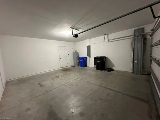 Garage featuring electric water heater, electric panel, and a garage door opener