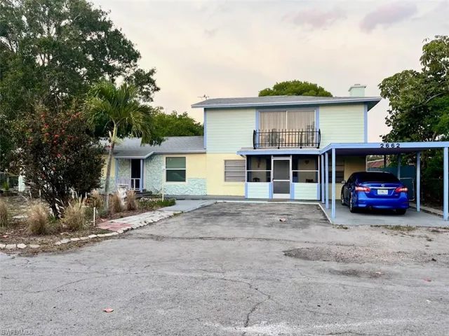 View of front of house with a balcony, an attached carport, asphalt driveway, and a chimney