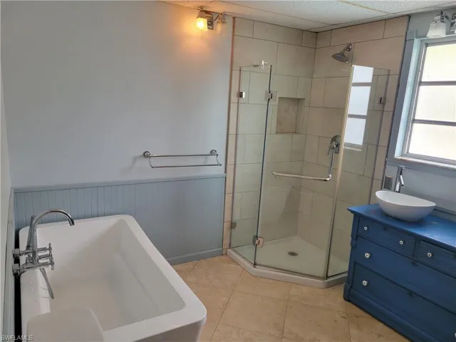 Bathroom featuring a soaking tub, vanity, a stall shower, a wainscoted wall, and light tile patterned flooring