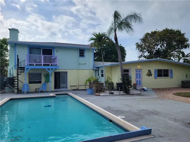 Rear view of property featuring a patio, a chimney, an outdoor pool, uncovered parking, and a balcony