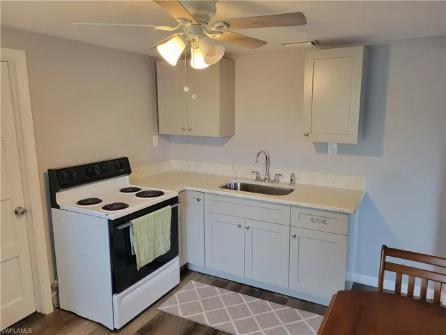 Kitchen with white electric stove, light stone counters, a ceiling fan, dark wood-style floors, and white cabinets