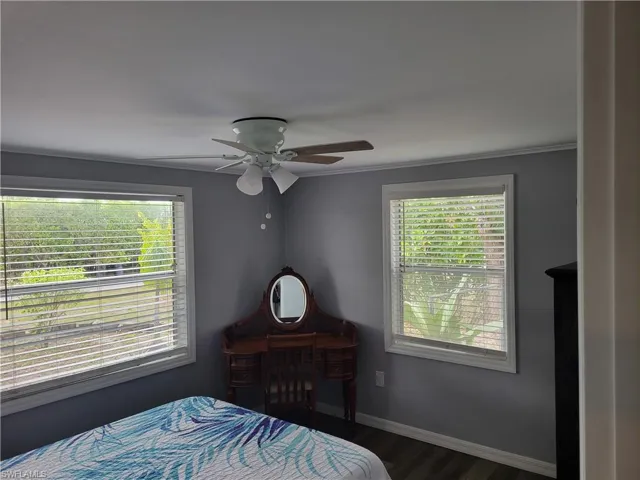 Bedroom with dark wood-type flooring, multiple windows, and ceiling fan