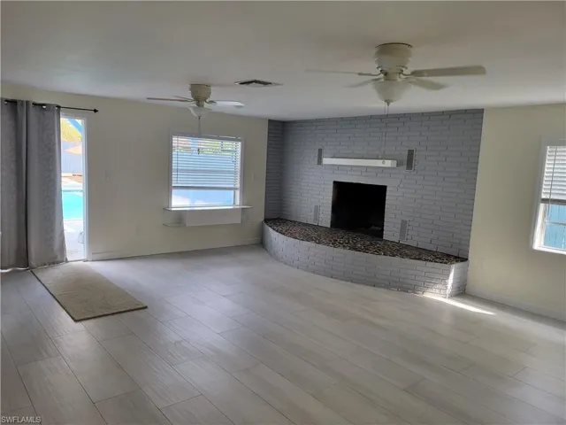 Unfurnished living room featuring ceiling fan, a brick fireplace, and light wood-type flooring