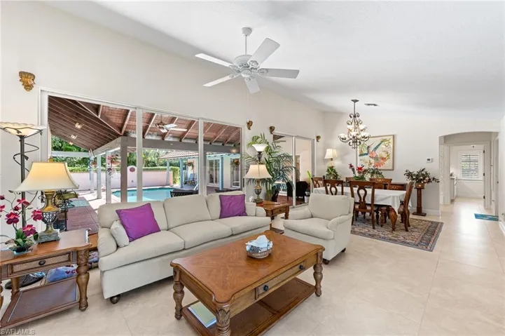 Living area with arched walkways, ceiling fan, light tile patterned floors, and high vaulted ceiling