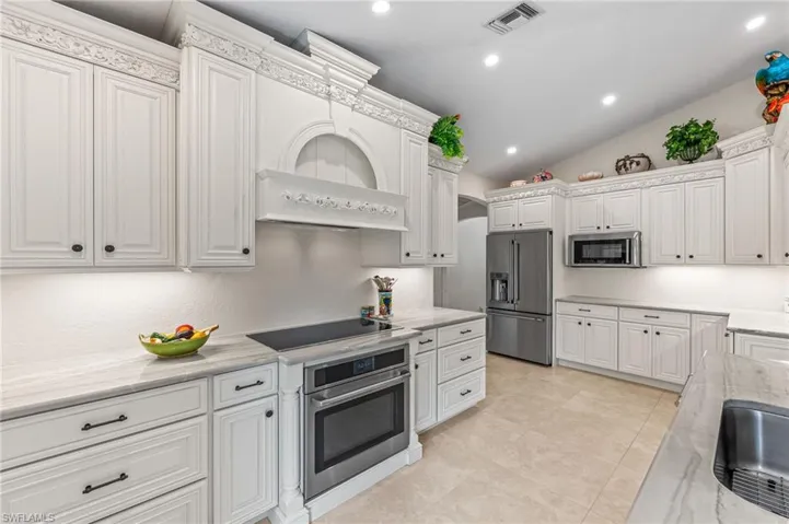 Kitchen featuring appliances with stainless steel finishes, custom range hood, white cabinets, lofted ceiling, and recessed lighting