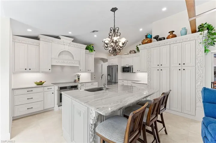 Kitchen with light stone countertops, arched walkways, a breakfast bar, hanging light fixtures, and vaulted ceiling