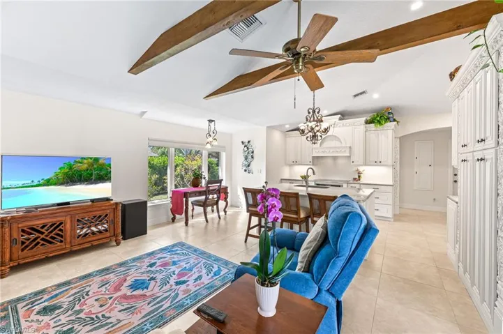 Living room featuring beamed ceiling, light tile patterned flooring, a ceiling fan, arched walkways, and high vaulted ceiling