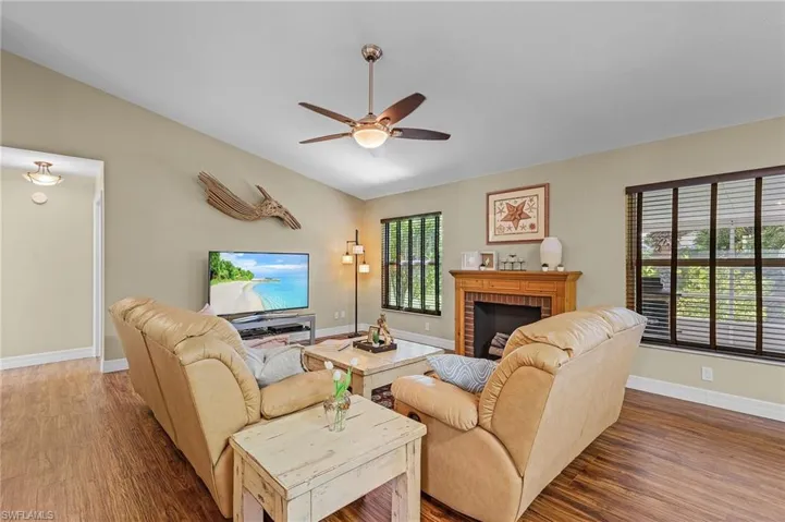 Living room with hardwood / wood-style floors, ceiling fan, a fireplace, and vaulted ceiling
