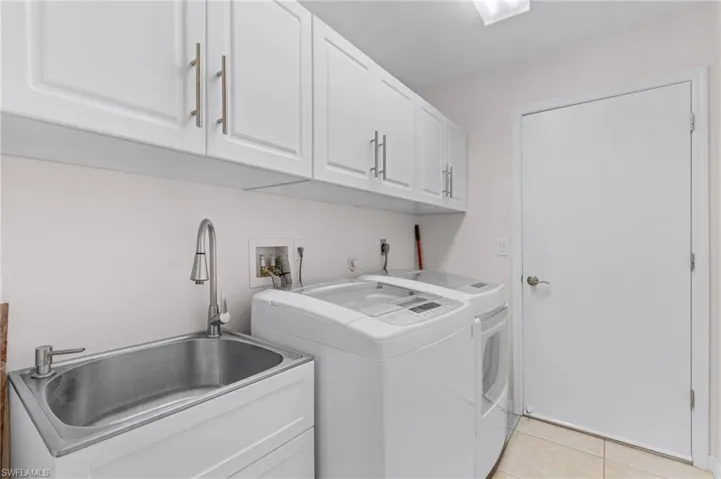 Clothes washing area featuring light tile patterned flooring, sink, cabinets, and separate washer and dryer