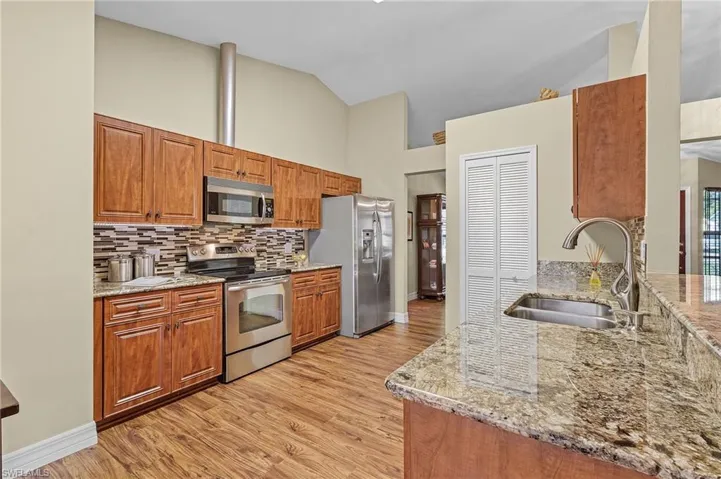 Kitchen with light stone countertops, light hardwood / wood-style flooring, backsplash, appliances with stainless steel finishes, and sink