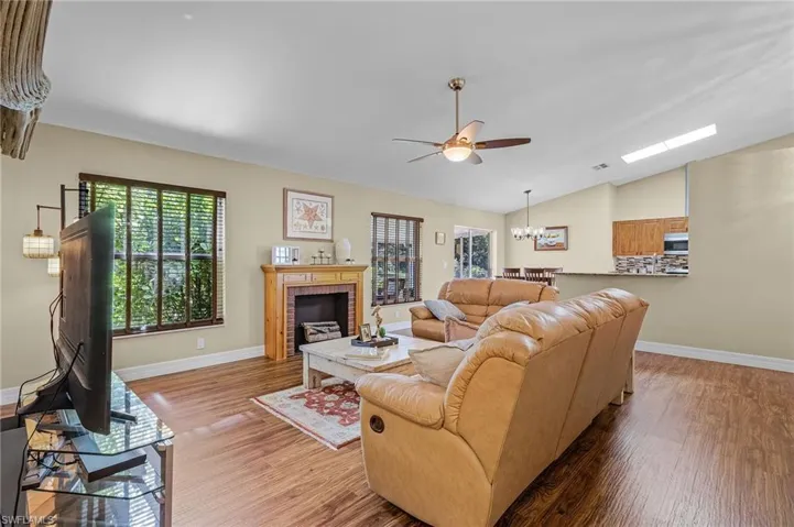 Living room with ceiling fan with notable chandelier, lofted ceiling, a brick fireplace, and hardwood / wood-style floors
