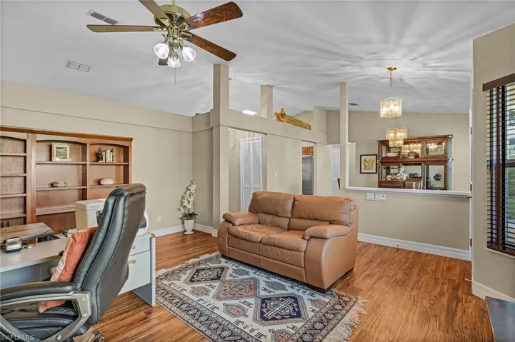 Home office with lofted ceiling, ceiling fan with notable chandelier, and wood-type flooring