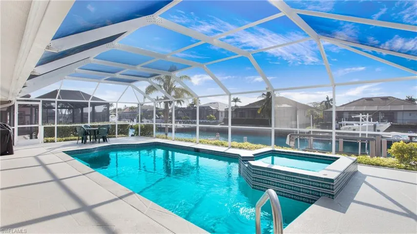 View of pool with glass enclosure, an in ground hot tub, a water view, and a patio