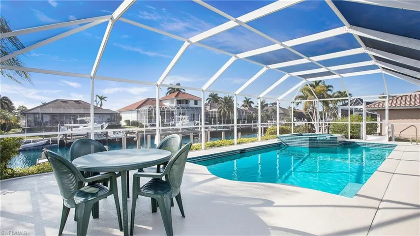 View of swimming pool featuring glass enclosure, an in ground hot tub, a patio area, and a water view