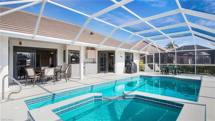 View of pool with glass enclosure, a patio area, and an in ground hot tub