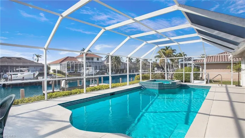 View of swimming pool with an in ground hot tub, a boat dock, a water view, glass enclosure, and a patio area