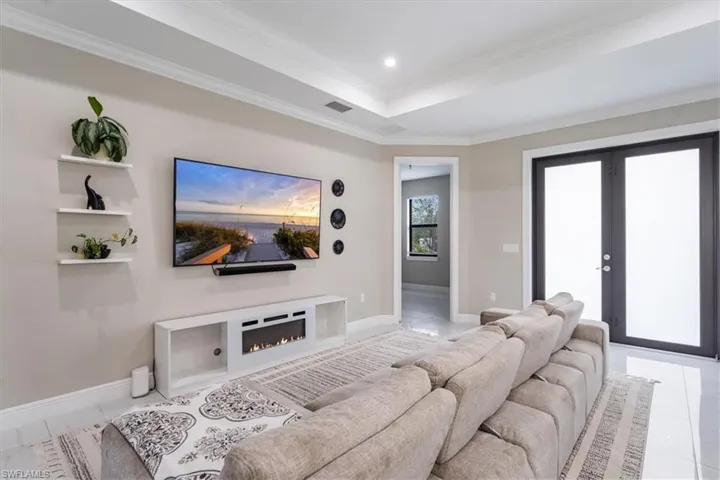 Living room with crown molding, a tray ceiling, french doors, recessed lighting, and a warm lit fireplace