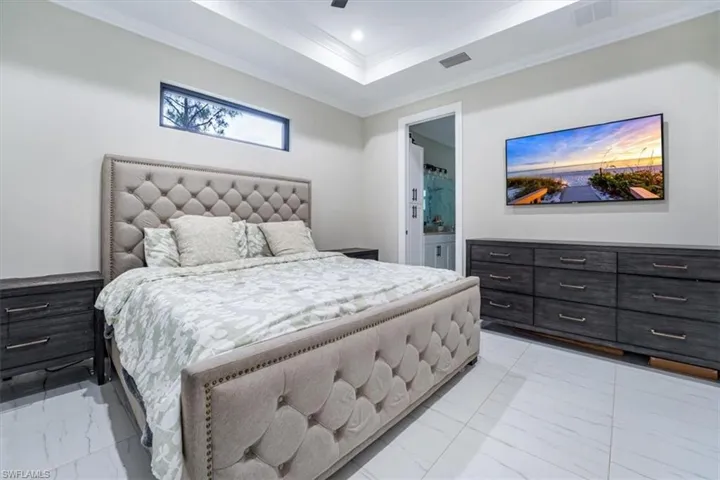 Bedroom with ornamental molding, light marble finish floors, a raised ceiling, connected bathroom, and recessed lighting
