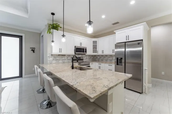 Kitchen with stainless steel appliances, a peninsula, glass insert cabinets, light stone counters, and white cabinets