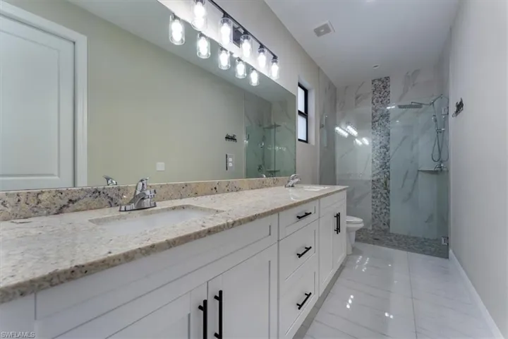 Full bath featuring a marble finish shower, tile patterned floors, and double vanity