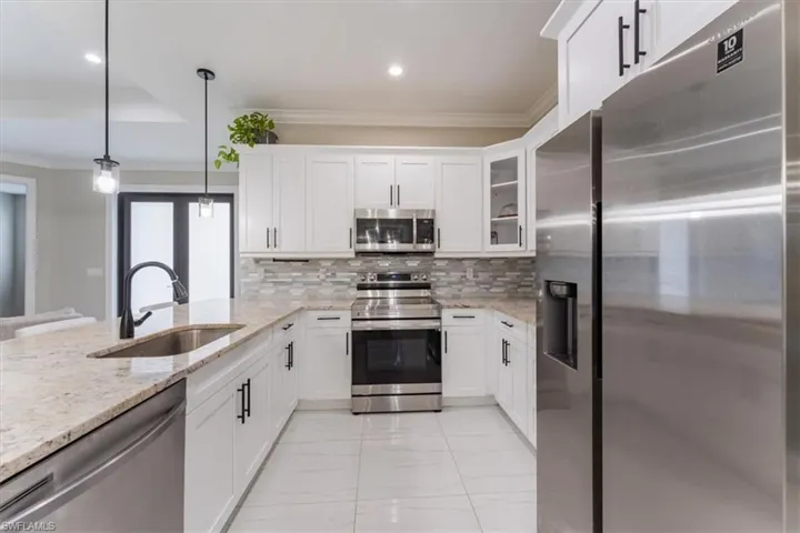 Kitchen featuring appliances with stainless steel finishes, light marble finish floors, white cabinets, crown molding, and tasteful backsplash