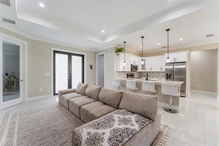 Living room featuring french doors, recessed lighting, light marble finish floors, crown molding, and a tray ceiling