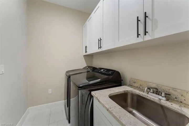 Laundry area featuring washing machine and clothes dryer, cabinet space, and marble finish floors