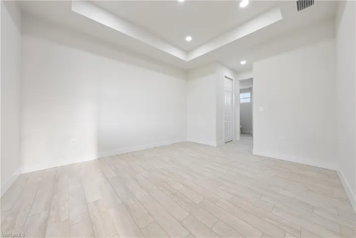 Empty room with a tray ceiling, light wood-style floors, and recessed lighting