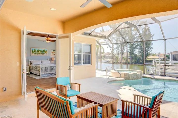 View of patio featuring a pool with connected hot tub, a ceiling fan, a lanai, and a water view