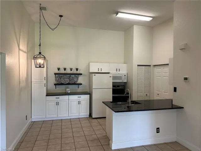 Kitchen featuring tile flooring, white cabinetry, black countertops, and a central island with an integrated sink