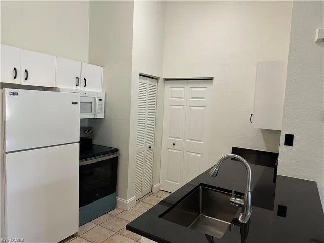 Kitchen featuring white cabinetry with black hardware, black countertops, stainless steel sink, and tile flooring