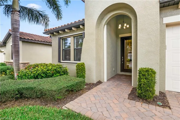 Elegant front of home with pavers walkway, lush greenery, and a 2-car garage.
