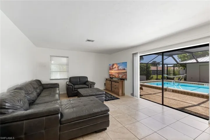 Living room area with tile flooring and slider out to the pool and screened lanai area.