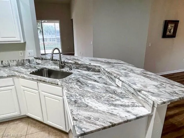 Kitchen featuring white cabinets, a peninsula, light stone counters, and light tile patterned flooring