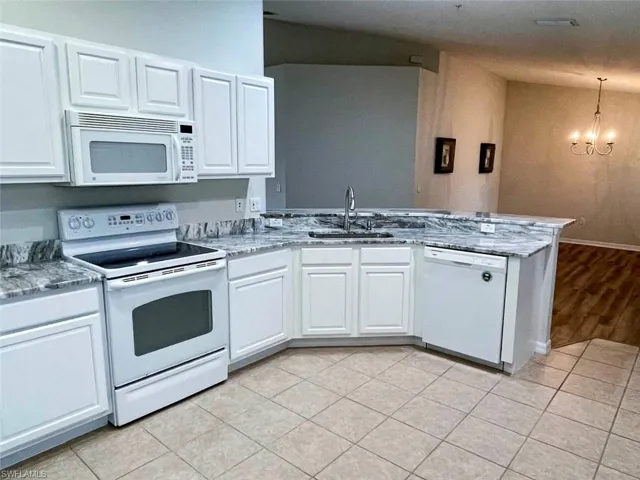 Kitchen featuring white appliances, white cabinets, a peninsula, hanging lights, and light tile patterned floors