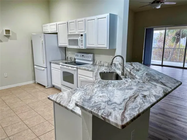 Kitchen with white appliances, a peninsula, white cabinets, ceiling fan, and a breakfast bar