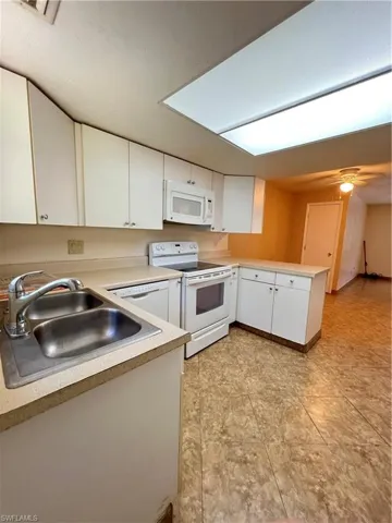 Kitchen featuring white appliances, a peninsula, white cabinets, and light countertops