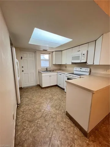 Kitchen featuring white cabinetry, white appliances, a skylight, light countertops, and a peninsula