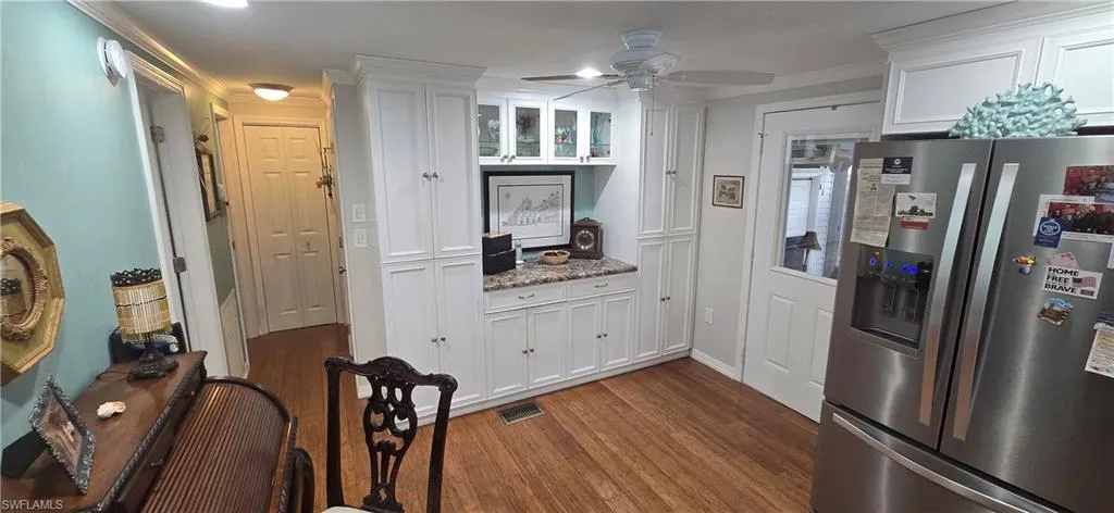 Kitchen featuring stainless steel fridge with ice dispenser, white cabinetry, wood finished floors, ceiling fan, and light stone countertops
